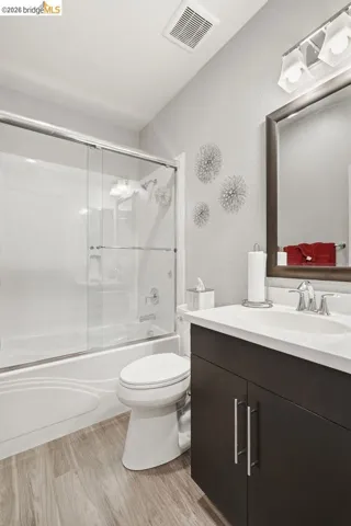 full bathroom with vanity, light wood finished floors, combined bath / shower with glass door, and a textured wall