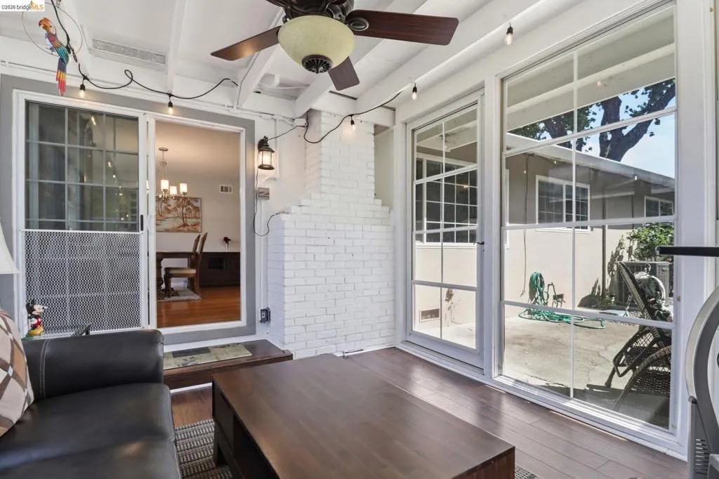 Screened patio featuring wood-finish flooring, a white painted brick wall, and a ceiling fan with integrated lighting