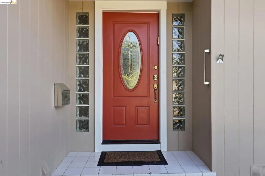 Red entry door with an oval-shaped glass insert, flanked by vertical glass block accents