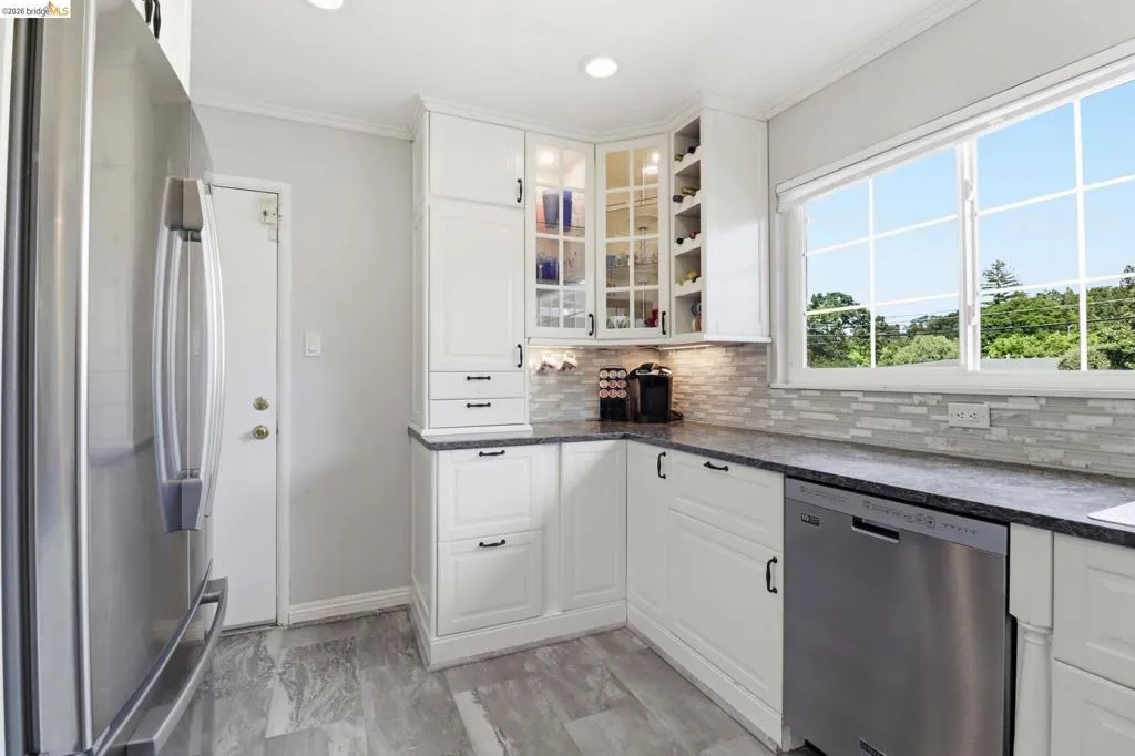 Kitchen featuring white cabinetry, dark countertops, a mosaic tile backsplash, stainless steel appliances, and wood-finish flooring