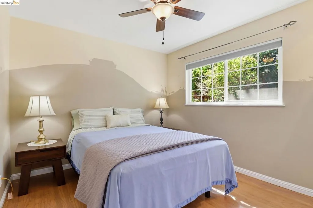 Bedroom featuring wood-finish flooring, a ceiling fan with integrated lighting, and a large window with multiple panes
