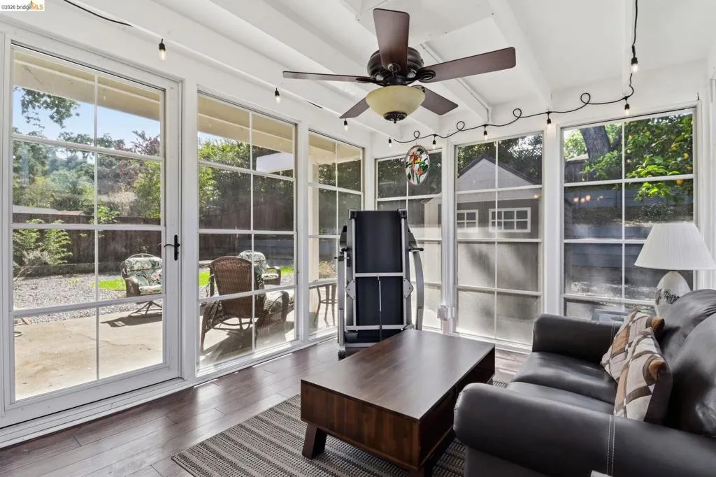 Sunroom featuring wood-finish flooring, exposed beam ceiling, and a ceiling fan