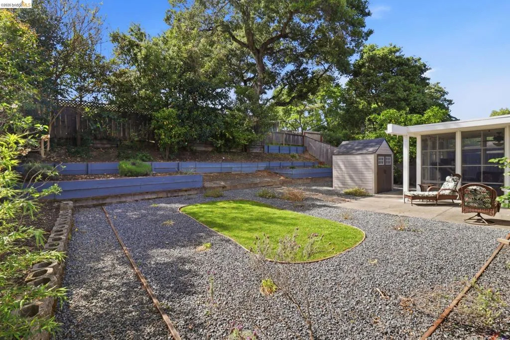 Spacious backyard featuring multiple tiered garden beds, a gravel-covered area, a manicured lawn section, a concrete patio, and a storage shed