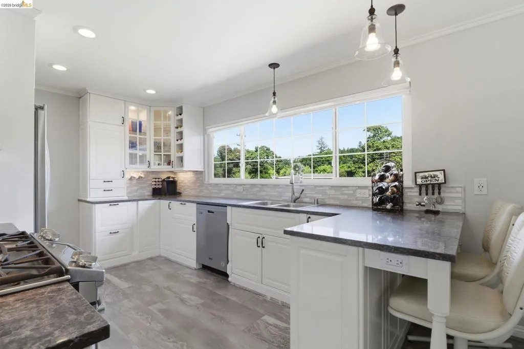 Bright kitchen featuring white cabinetry, grey stone countertops, wood-finish flooring, a tiled backsplash, and recessed lighting