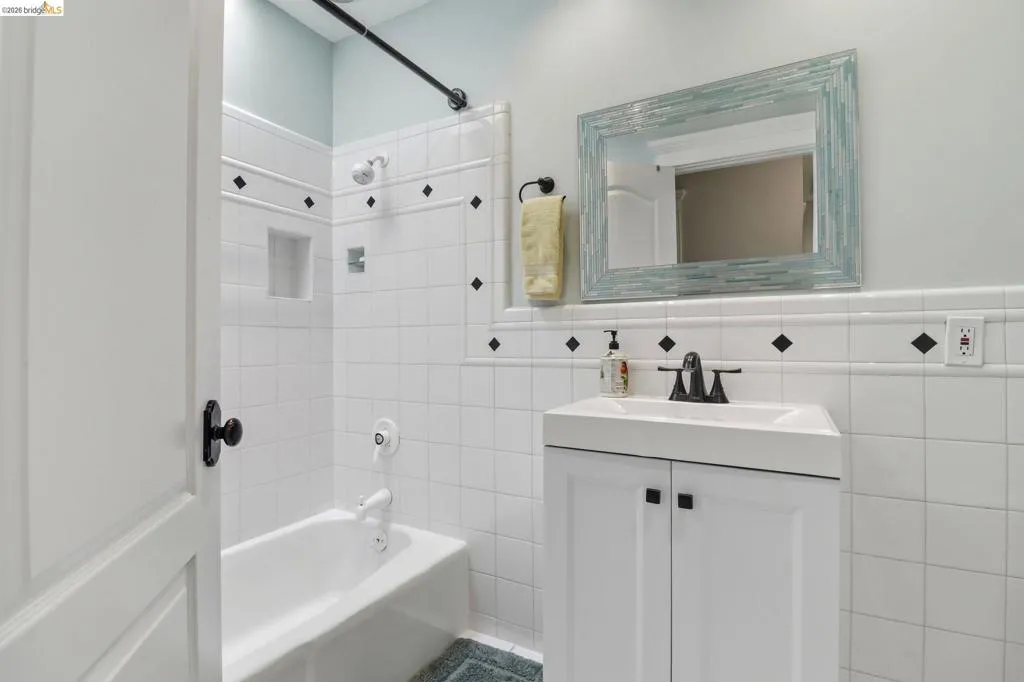 Bathroom featuring a white subway tile surround with black accent diamonds, a built-in shower niche, and a white vanity with integrated sink