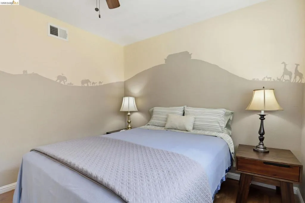 Bedroom featuring a ceiling fan, wood-finish flooring, and a two-tone wall treatment with a decorative motif