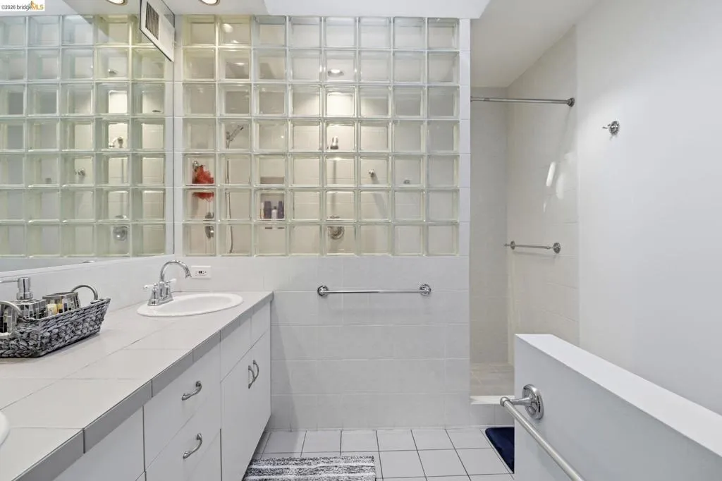 Bathroom featuring a glass block shower enclosure, white tiled walls, and a vanity with an integrated sink