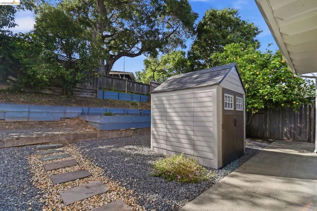 Backyard featuring a shed with double doors, a gravel and stone paver pathway, and tiered wood retaining walls