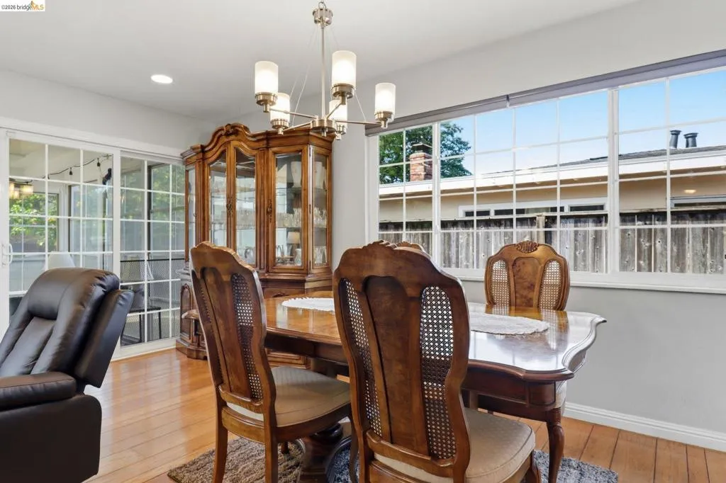 Dining area featuring wood-finish flooring, a contemporary chandelier, recessed lighting, and large windows with grid patterns