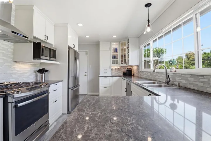 Kitchen featuring extensive gray countertop space, white cabinetry, stainless steel appliances, and a large multi-pane window