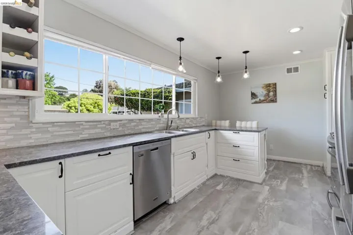 Kitchen featuring white cabinetry, dark countertops, a large window, stainless steel dishwasher, and pendant lighting