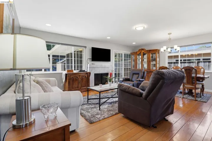 Open concept living and dining area featuring wood-finish flooring, a white mantel fireplace, and recessed lighting