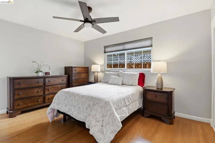 Room featuring wood-finish flooring, a ceiling fan with integrated lighting, and a window with blinds