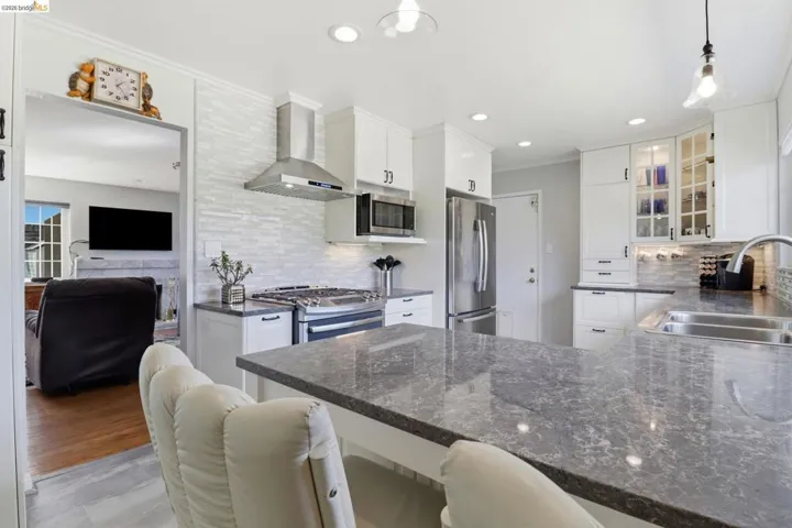 Modern kitchen featuring white cabinetry, stainless steel appliances, a tile backsplash, recessed lighting, and a kitchen island with stone countertops