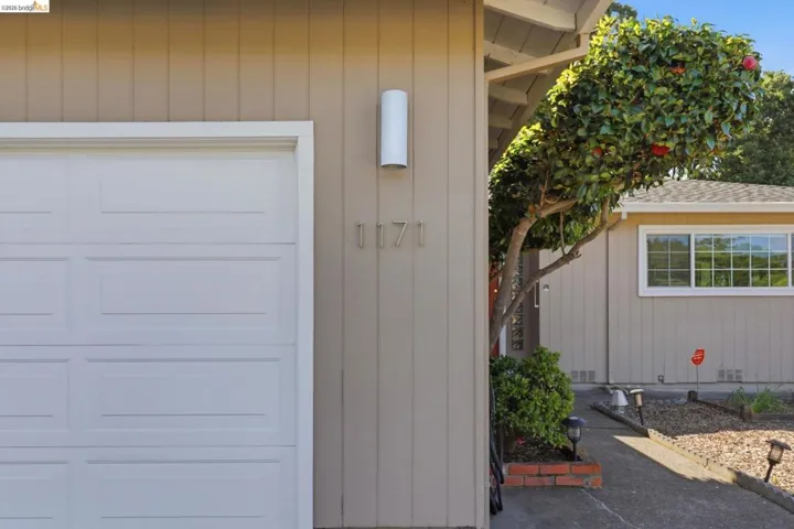 Exterior with panel siding, a white sectional garage door, and a cylindrical outdoor light fixture