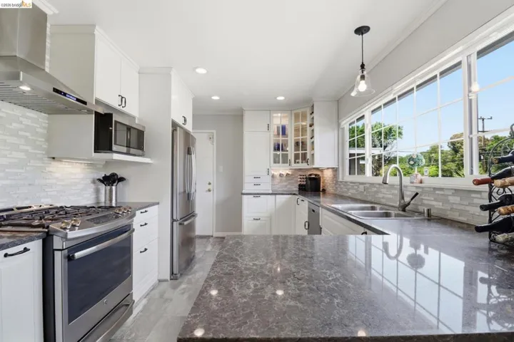Contemporary kitchen featuring stone countertops, white shaker cabinetry, stainless steel appliances, a tiled backsplash, and recessed lighting