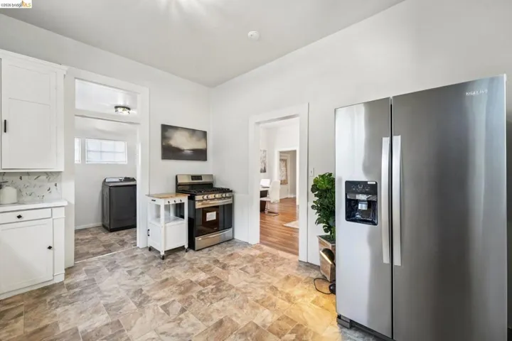 Kitchen with appliances with stainless steel finishes, white cabinetry, washer / clothes dryer, and stone finish floors