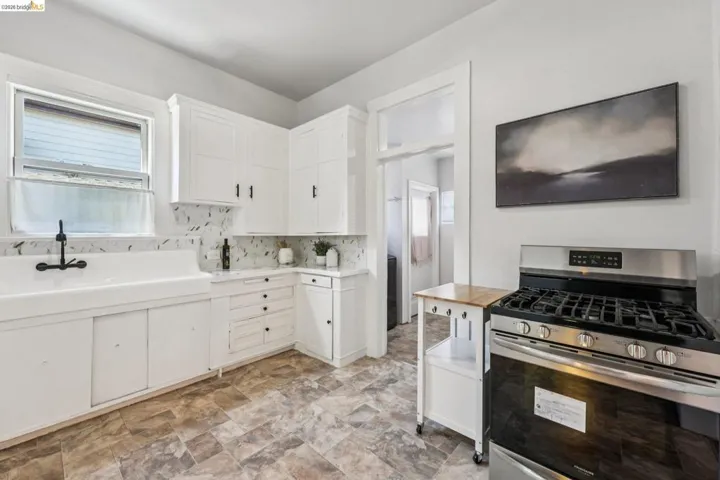Kitchen featuring stainless steel range with gas cooktop, white cabinets, healthy amount of natural light, and stone finish floors