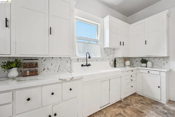 Kitchen with white cabinetry, stone finish floors, decorative backsplash, and light stone counters