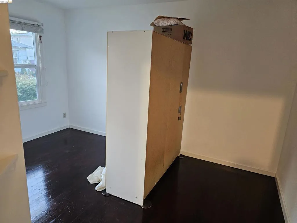 Room featuring dark wood-finish flooring, white baseboards, and a window with blinds providing natural light