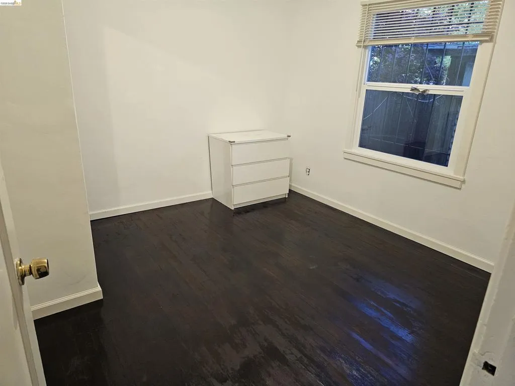 Dark wood-finish flooring with white baseboards and neutral wall paint