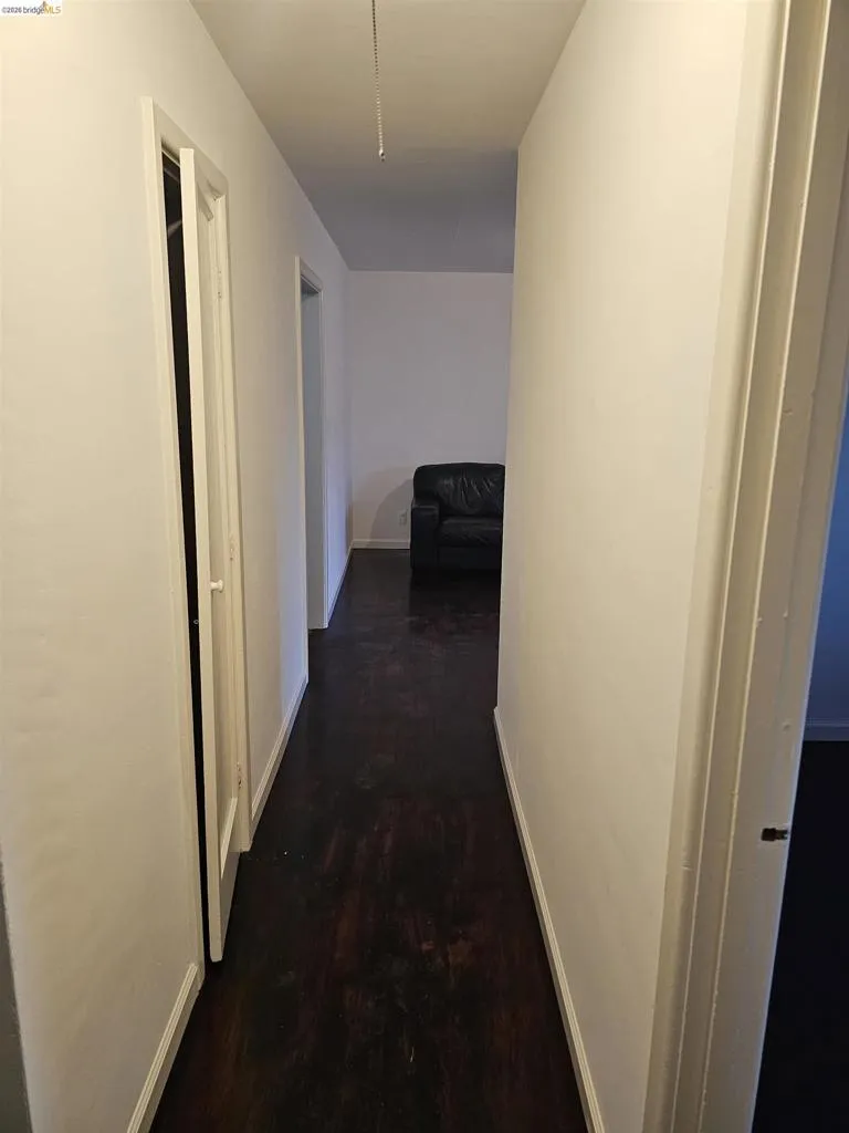 Hallway featuring dark wood-finish flooring, white painted walls, and white trim molding