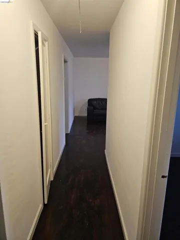 Hallway featuring dark wood-finish flooring, white painted walls, and white trim molding