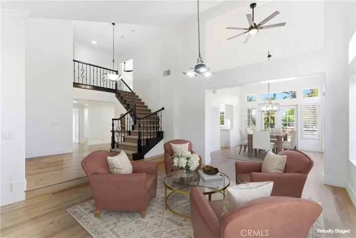 Virtually staged. Bright and airy living space with soaring ceilings, elegant staircase, and abundant natural light, flowing seamlessly into the dining area.