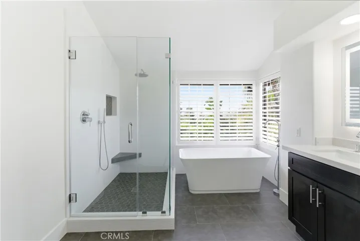 Beautifully remodeled primary bath featuring a freestanding tub, glass-enclosed shower, and dual sinks.