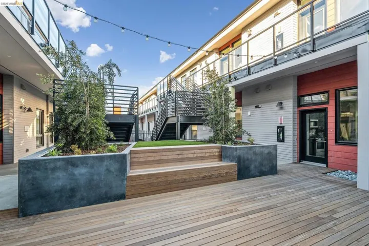 Expansive outdoor deck featuring wood-finish flooring, a tiered concrete and wood-finish planter with mature trees, and string lighting overhead