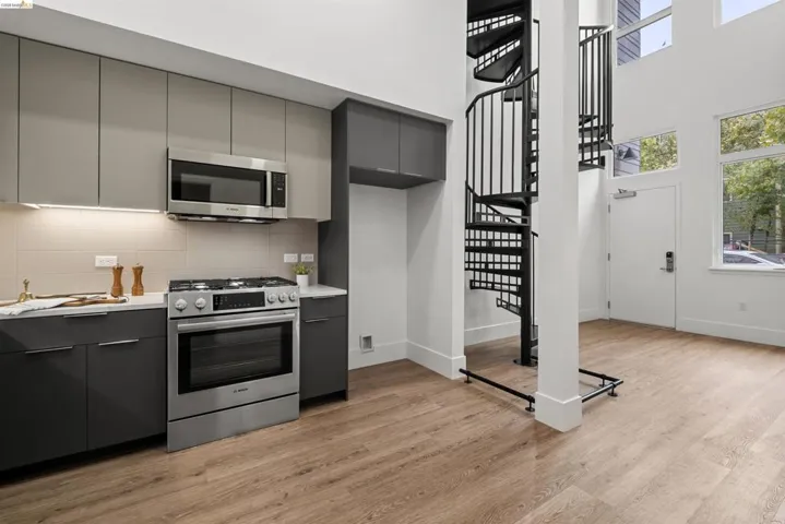 Kitchen with gray cabinets, modern cabinets, stainless steel appliances, light countertops, and a high ceiling