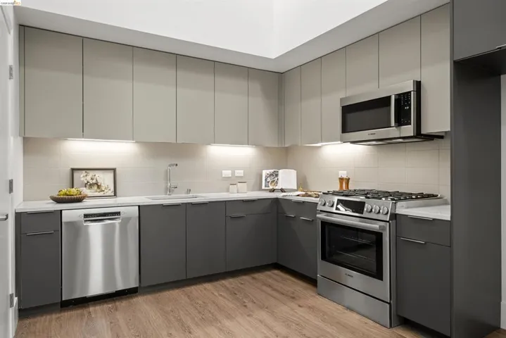 Kitchen with gray cabinets, appliances with stainless steel finishes, modern cabinets, and light wood finished floors