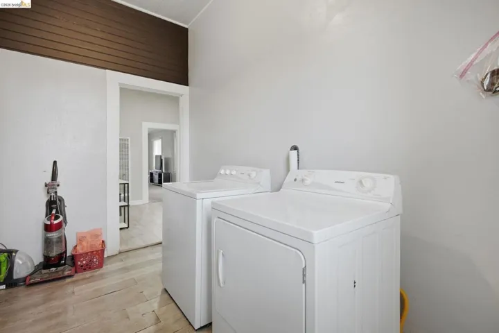 Dedicated laundry area featuring a washer and dryer, light wood-finish flooring, and a distinct brown wood-paneled accent wall