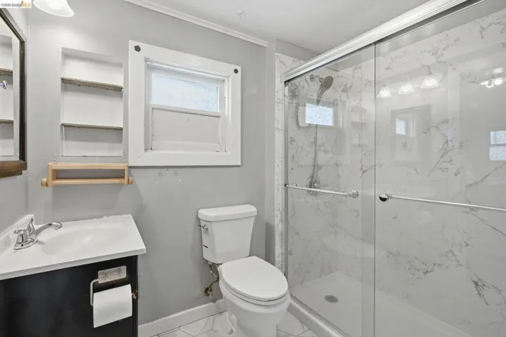 Bathroom featuring a glass-enclosed shower with white marble-patterned wall tiles, a white porcelain toilet, a dark wood-finish vanity with an integrated sink, and hexagon-patterned floor tiles