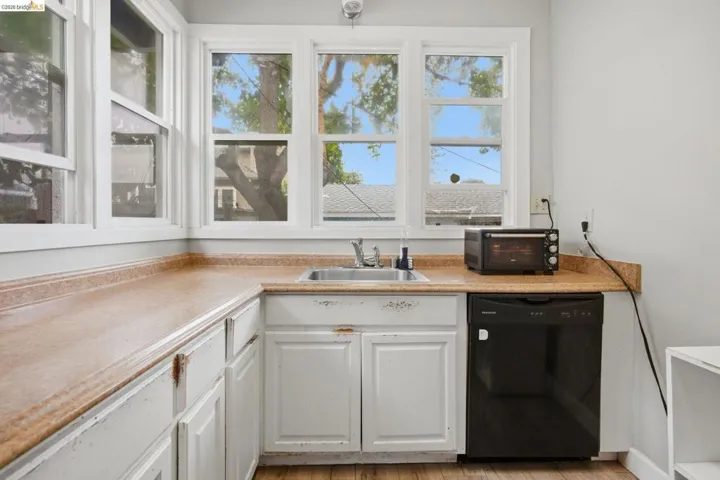 Kitchen featuring wrap-around countertops, a stainless steel sink, white cabinetry, a black dishwasher, and wood-finish flooring