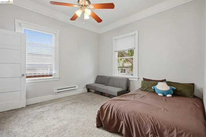 Carpeted room featuring a ceiling fan with light fixture, two windows, and a wall-mounted heater