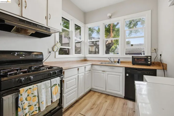 Kitchen featuring white cabinetry, light wood-finish flooring, and a corner sink with a window array