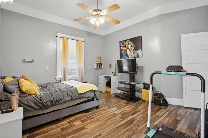 Bedroom featuring wood-finish flooring, a ceiling fan with integrated lighting, and a white-trimmed window