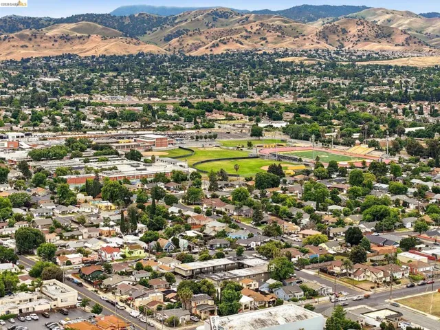 Aerial view showcasing an expansive residential area with varied rooflines and mature tree cover, set against a backdrop of rolling hills