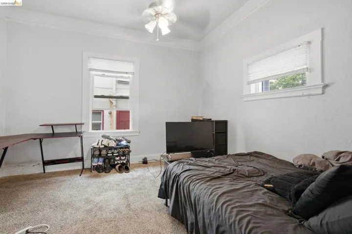 Light-filled room featuring textured walls, two windows with blinds, a ceiling fan with light fixture, decorative crown molding, and carpeted flooring