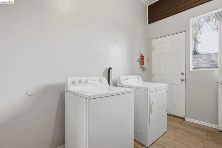 Utility room featuring a white paneled exterior door, wood-finish flooring, and slatted window blinds