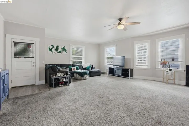 Spacious living area featuring light gray carpet, multiple windows with white trim, and a ceiling fan with integrated lighting