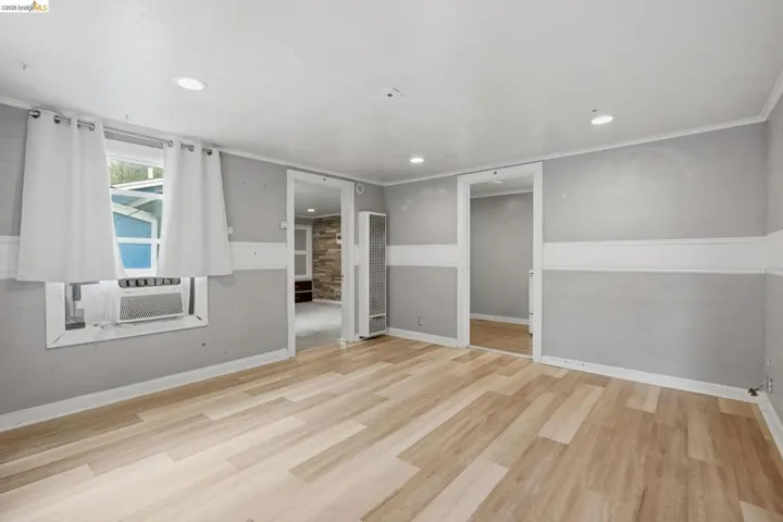 Spacious room featuring wood-finish flooring, light gray walls with white wainscoting, recessed ceiling lighting, and a wall-mounted heating unit