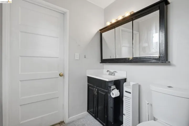 Bathroom featuring a white paneled door, a dark wood-finish vanity with an integrated sink, a chrome-finish faucet, a dark wood-finish mirrored medicine cabinet, and a white toilet