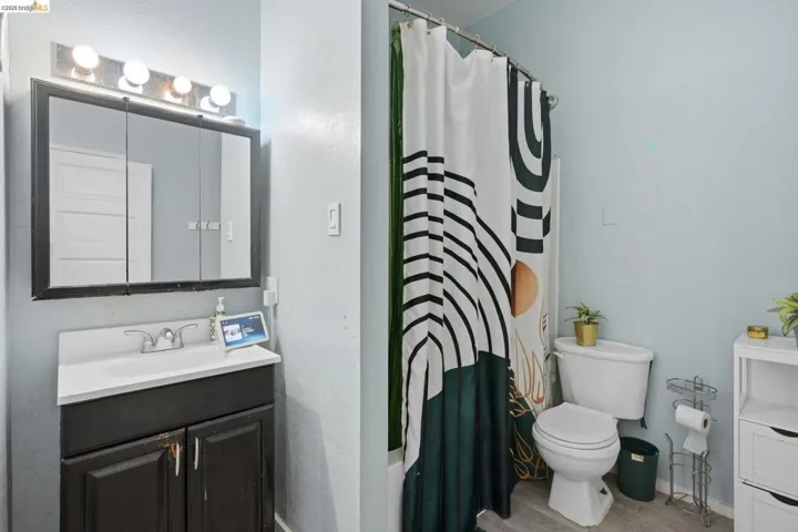 Bathroom featuring a single vanity with a white countertop, a medicine cabinet with integrated lighting, a toilet, and wood-finish flooring