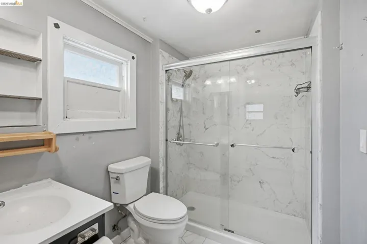 Walk-in shower with clear glass enclosure and marble-look surround, alongside a built-in vanity with integrated sink