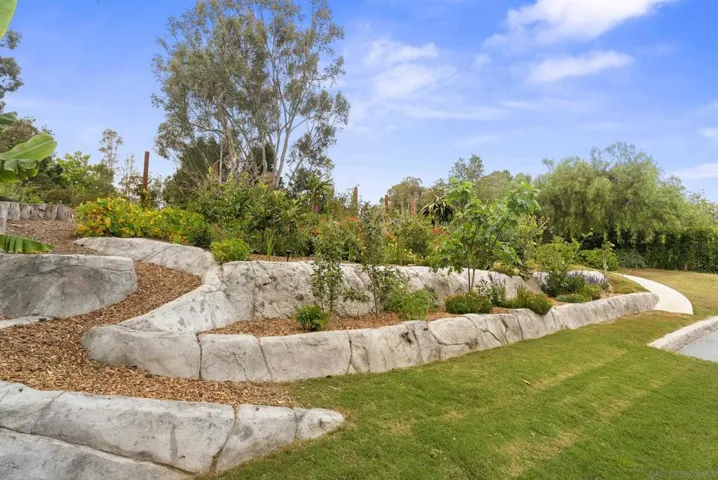 Lush curated gardens and layered greenery surround the estate, where sculpted stone terraces, mature trees, and vibrant plantings create a peaceful outdoor setting rich in texture, privacy, and natural beauty.