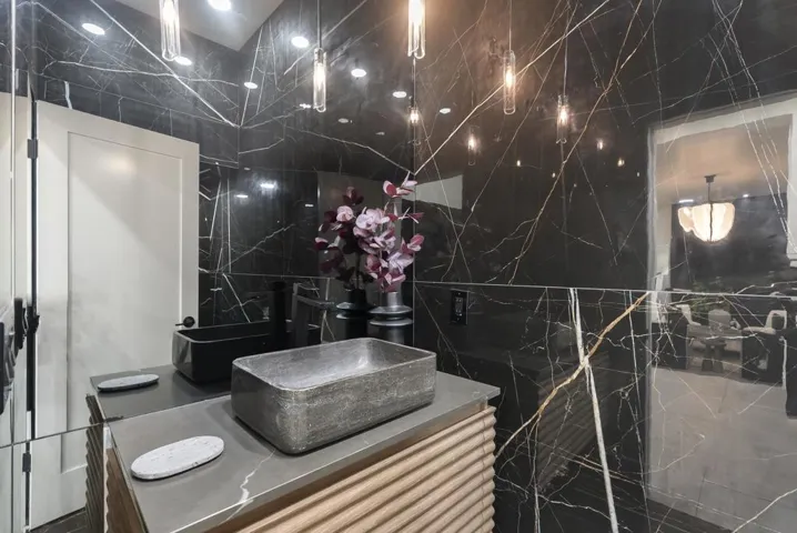 A dramatic designer powder bath wrapped in floor to ceiling black stone, where striking veining, sculptural lighting, and a bold modern vanity create a moody, gallery-inspired statement.