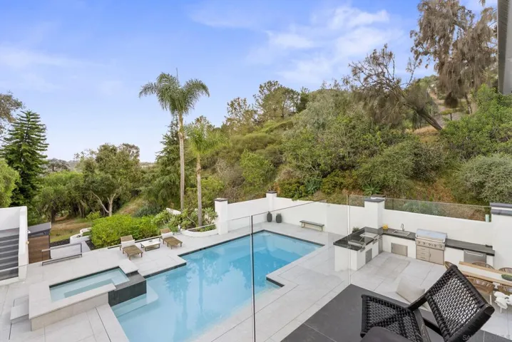 The private balcony off the primary suite overlooks a resort-style pool and spa framed by lush hillside surroundings, creating a peaceful retreat designed for morning coffee, sunset evenings, and effortless indoor outdoor living.