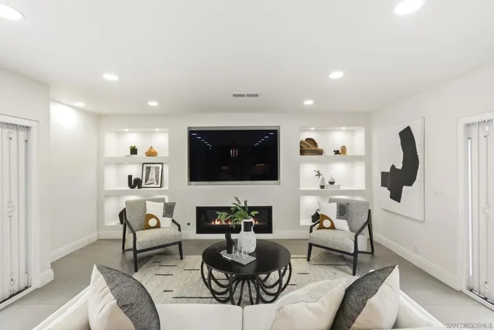 An inviting living space flowing seamlessly from the kitchen, where a sleek modern fireplace, custom illuminated shelving, and a refined neutral palette create the perfect setting for effortless everyday living and entertaining.